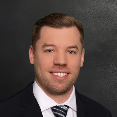 Chiropractor Ryan Weyenberg Smiling In Black Suit With Grey Shirt